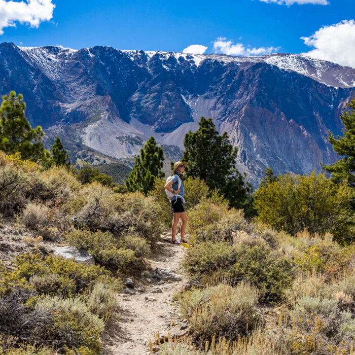A woman stands on a trail in front of mountains.